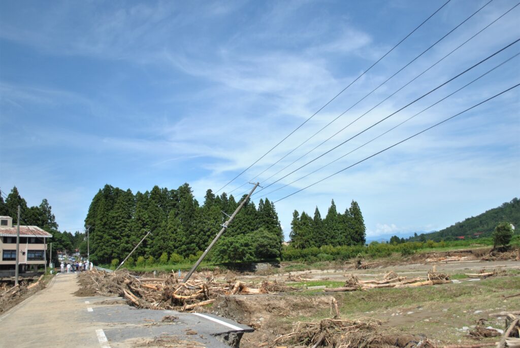 大巻橋が崩落した付近では、電柱が斜めに大きく傾き、根こそぎ流された木が何本も道路に押し寄せていました。（8月6日、飯豊町）